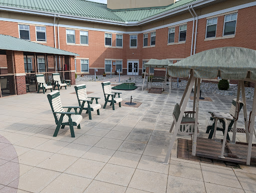 A spacious courtyard with green outdoor seating and sunshades, surrounded by a brick building.