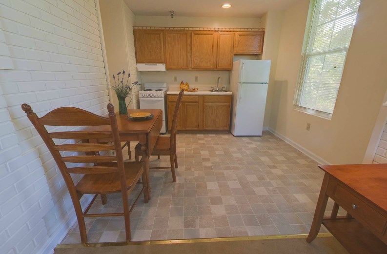 A cozy kitchen and dining area featuring wooden cabinets, a small table with chairs, a refrigerator, and a stove.