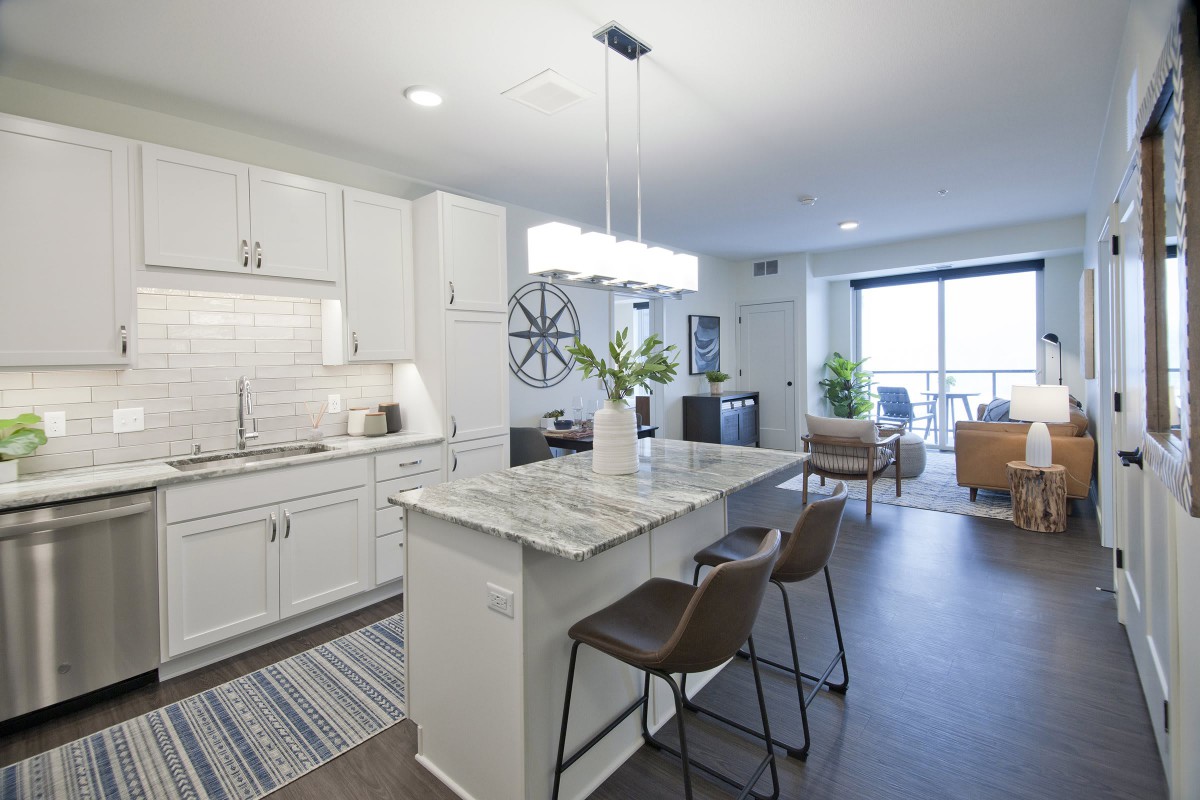 A modern open-plan kitchen with a central island and bar stools, leading into a cozy living and dining area.