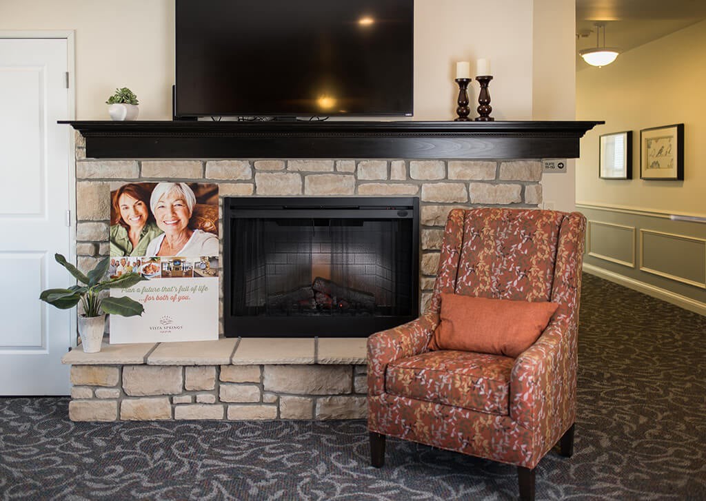 A cozy living room setup featuring a stone fireplace, television, patterned armchair, and decorative candles.