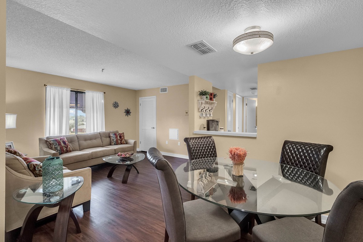 A modern living and dining area with a glass table, sofa, and wooden flooring.