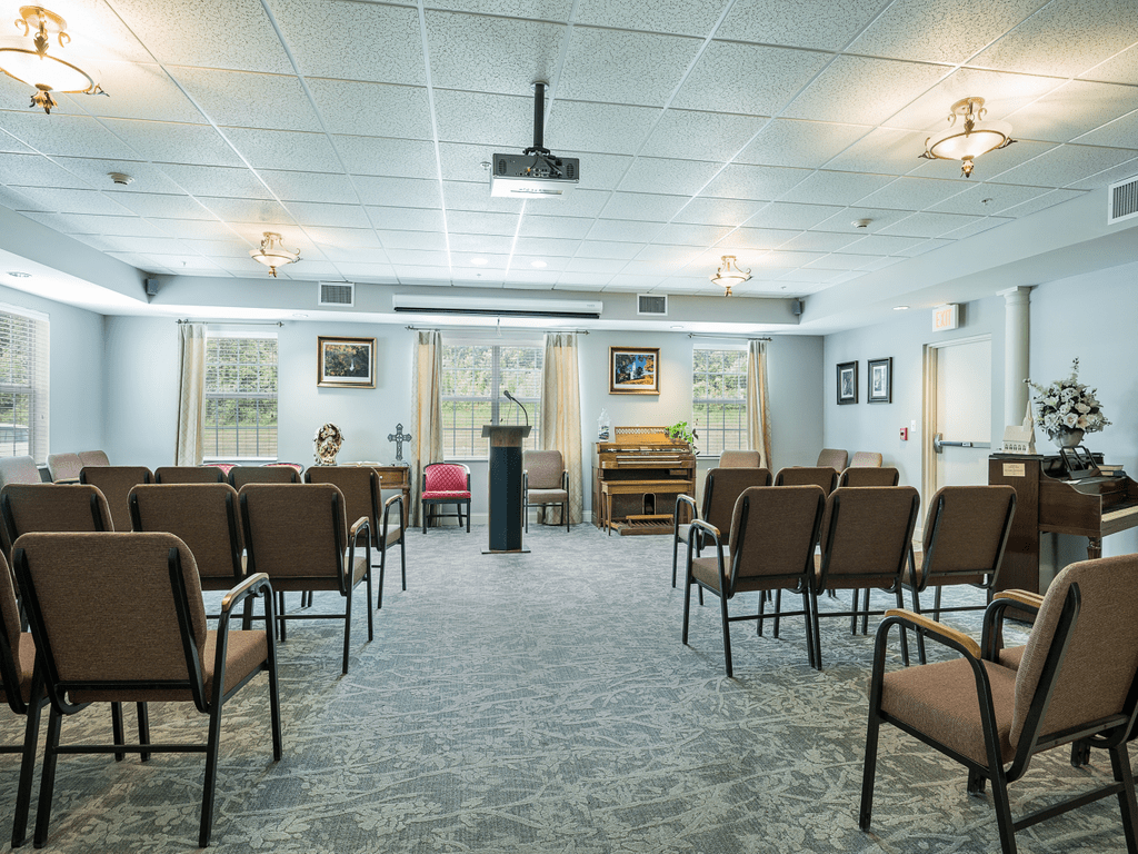 A room set up for a small gathering with rows of chairs facing a podium and projector.