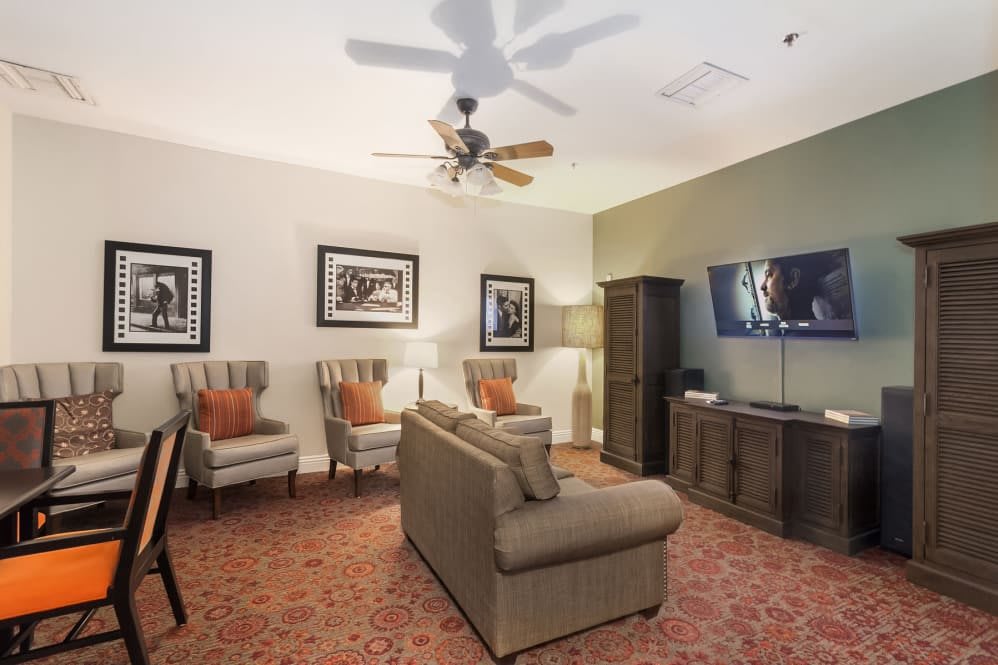 A cozy living room with comfortable seating and modern decor, featuring a television and ceiling fan.