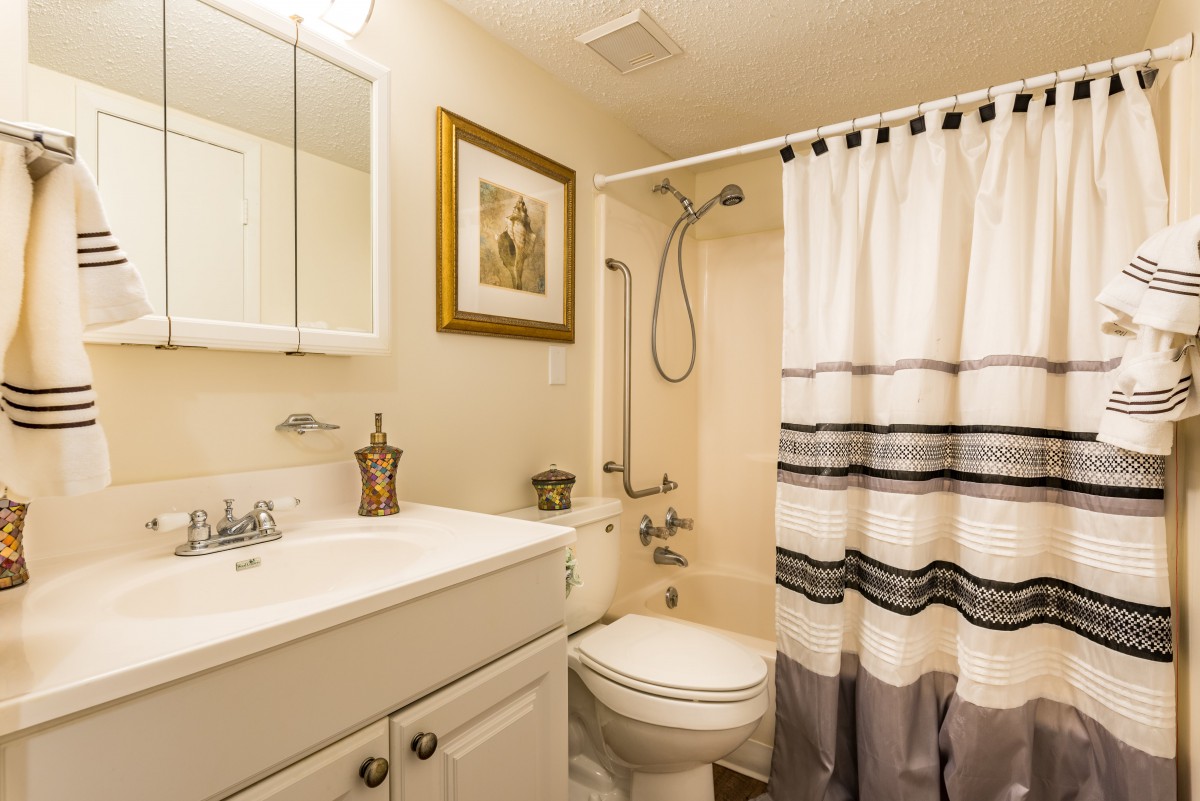 A cozy and well-lit bathroom with a sink, mirror cabinet, toilet, and shower with a patterned curtain.