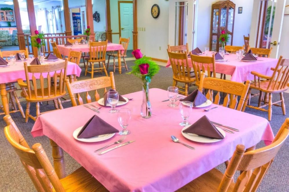 A cozy restaurant dining area with tables set for guests, featuring pink tablecloths and roses in vases.