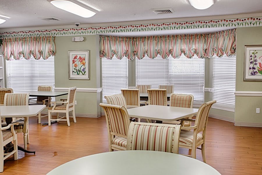 A well-lit dining area with multiple tables and chairs, decorated with curtains and wall art.