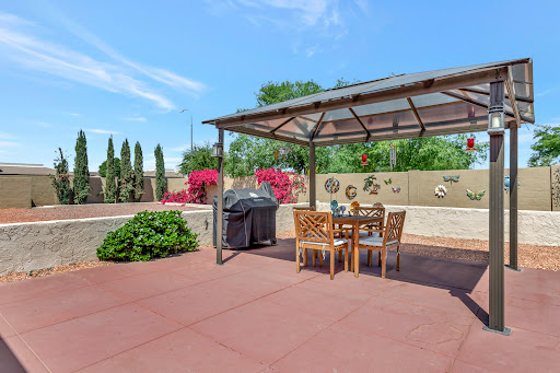 A cozy outdoor dining area featuring a stylish pergola, a grill, and beautiful landscaping.