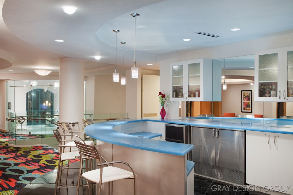 A modern kitchen with a blue countertop and pendant lighting, featuring bar stools and an open design.