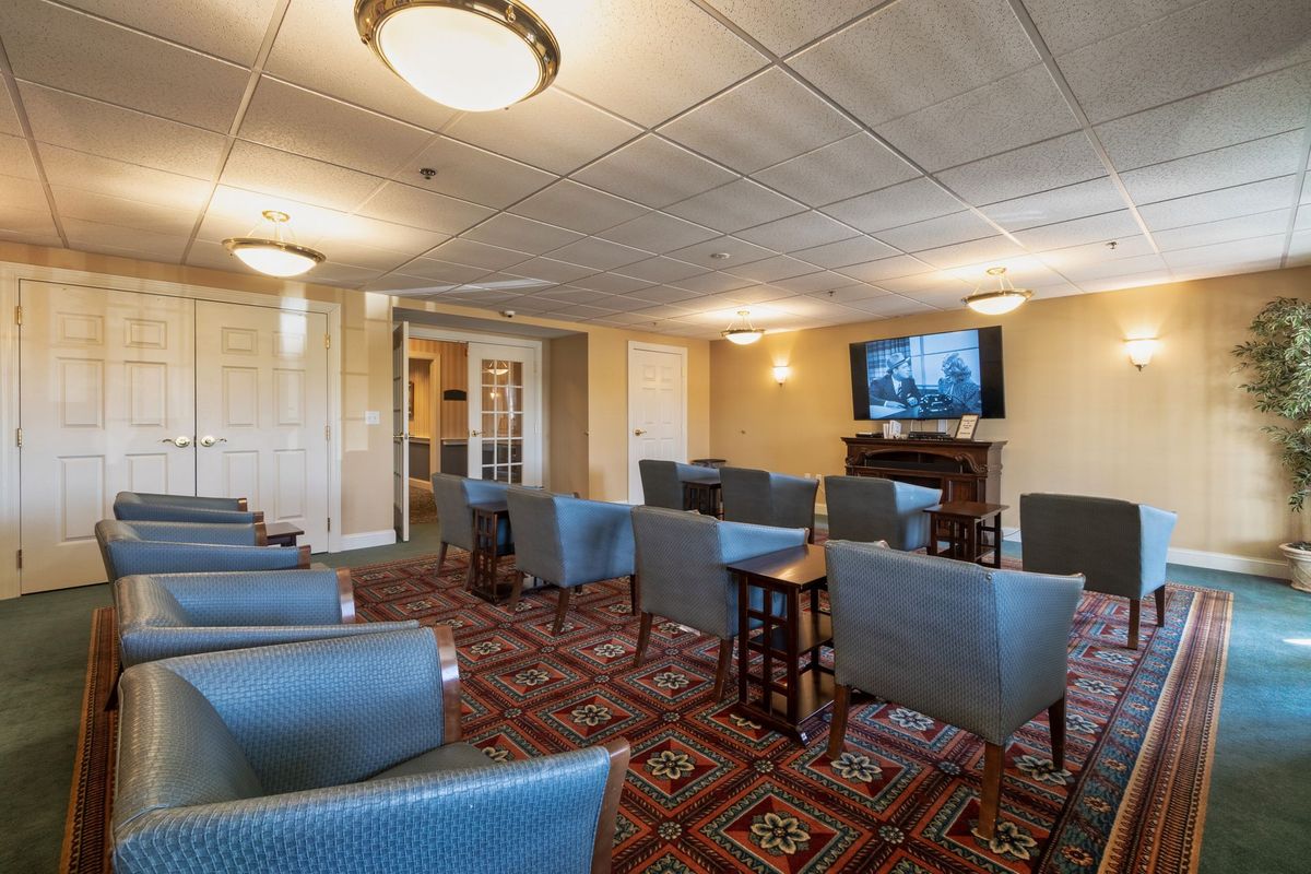 A comfortable lounge area with multiple chairs facing a television, featuring warm lighting and a patterned carpet.