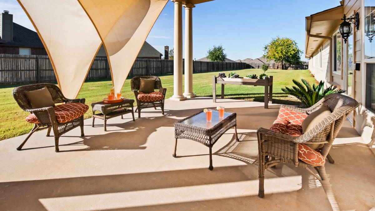 A sunny patio with stylish outdoor furniture and a shade sail overlooking a spacious backyard.