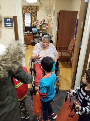Children visiting an elderly woman in a care facility, sharing moments of joy.