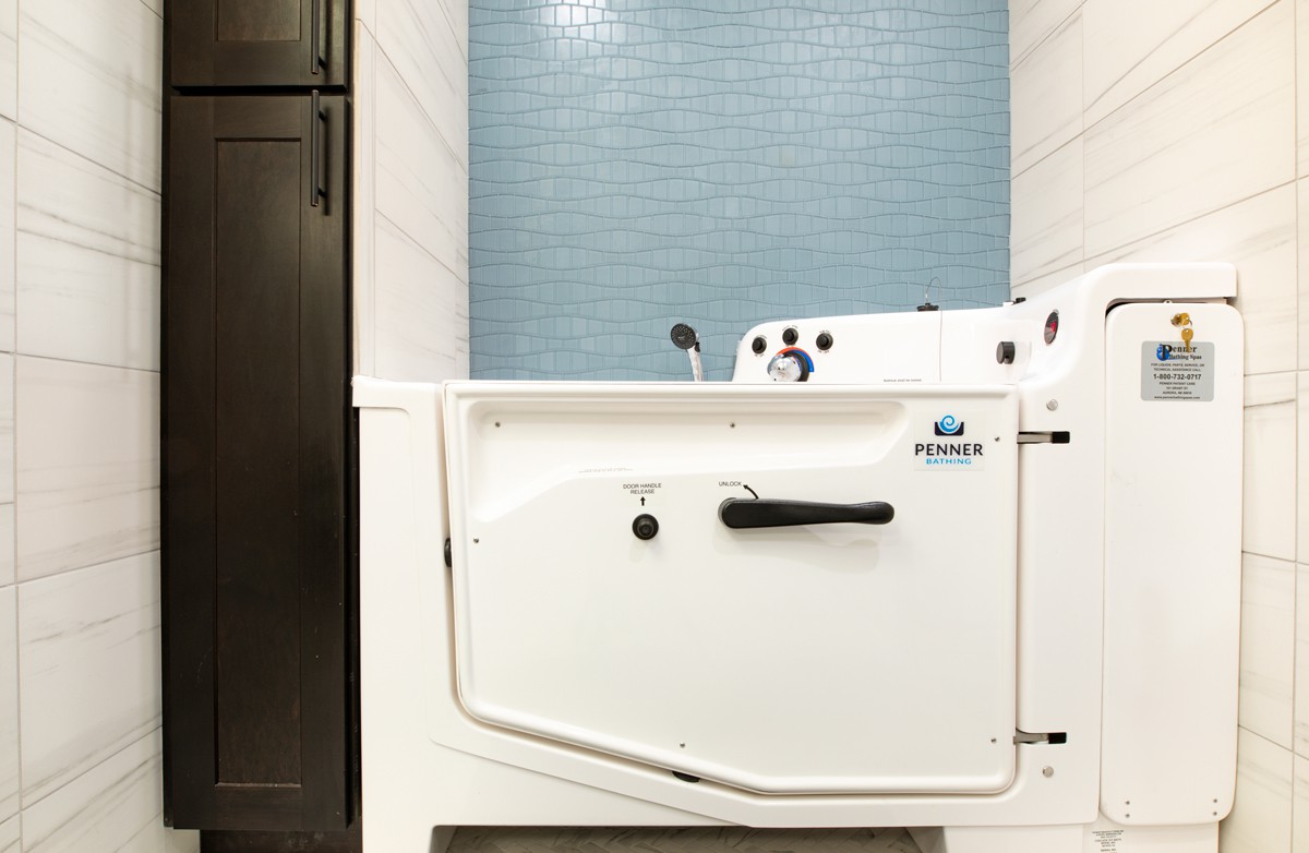 A walk-in bathtub with a door and blue tiled wall in a modern bathroom.
