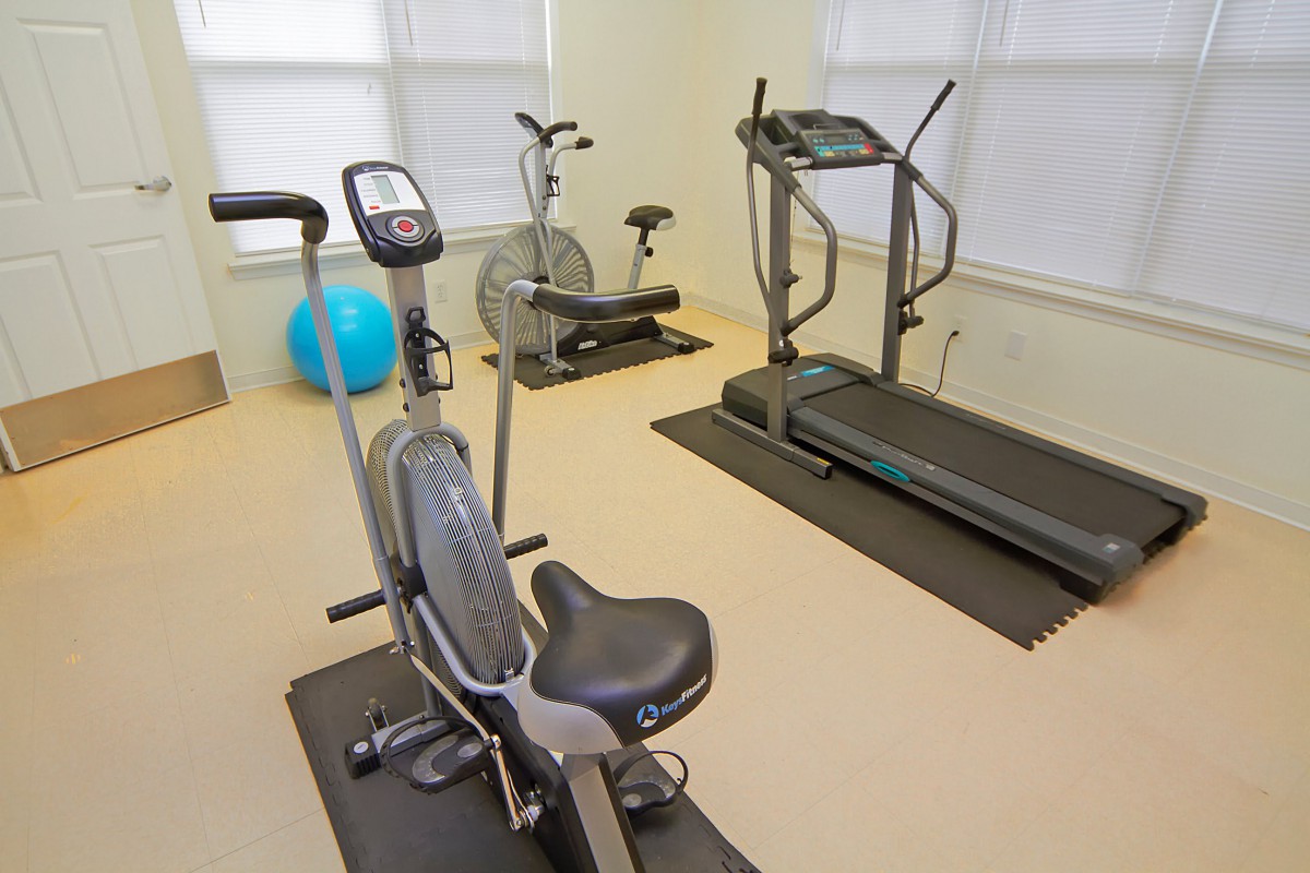 A small gym with various exercise equipment, including a treadmill, stationary bike, and elliptical machine.
