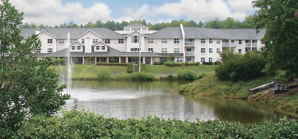 A scenic view of a large building by a tranquil lake surrounded by greenery.