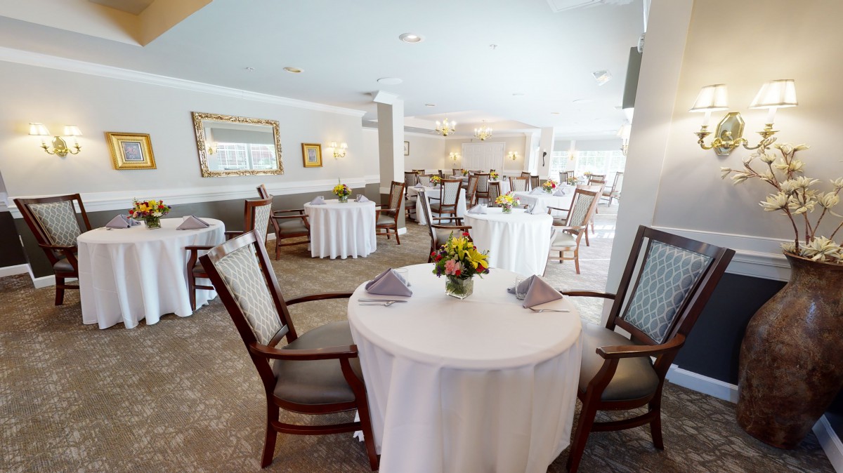 A beautifully set dining room with round tables, covered in white tablecloths and adorned with floral centerpieces.