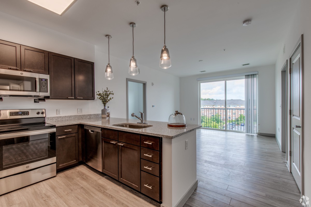 A modern kitchen with dark wooden cabinets and an island counter, featuring pendant lighting in an open and bright apartment space.