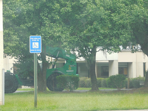 A green landscaping vehicle parked near a designated parking spot, surrounded by trees and grass.