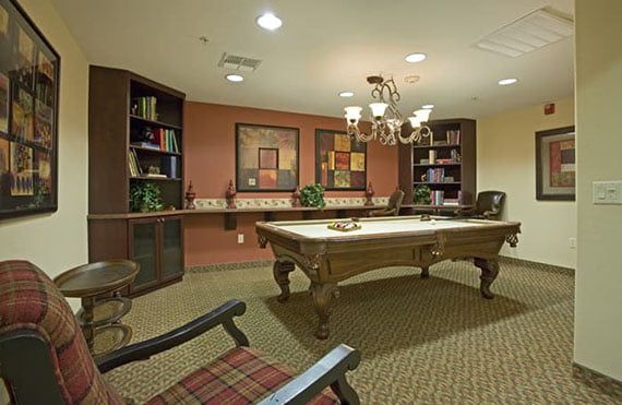 A cozy billiard room with a pool table, bookshelves, and a chandelier.