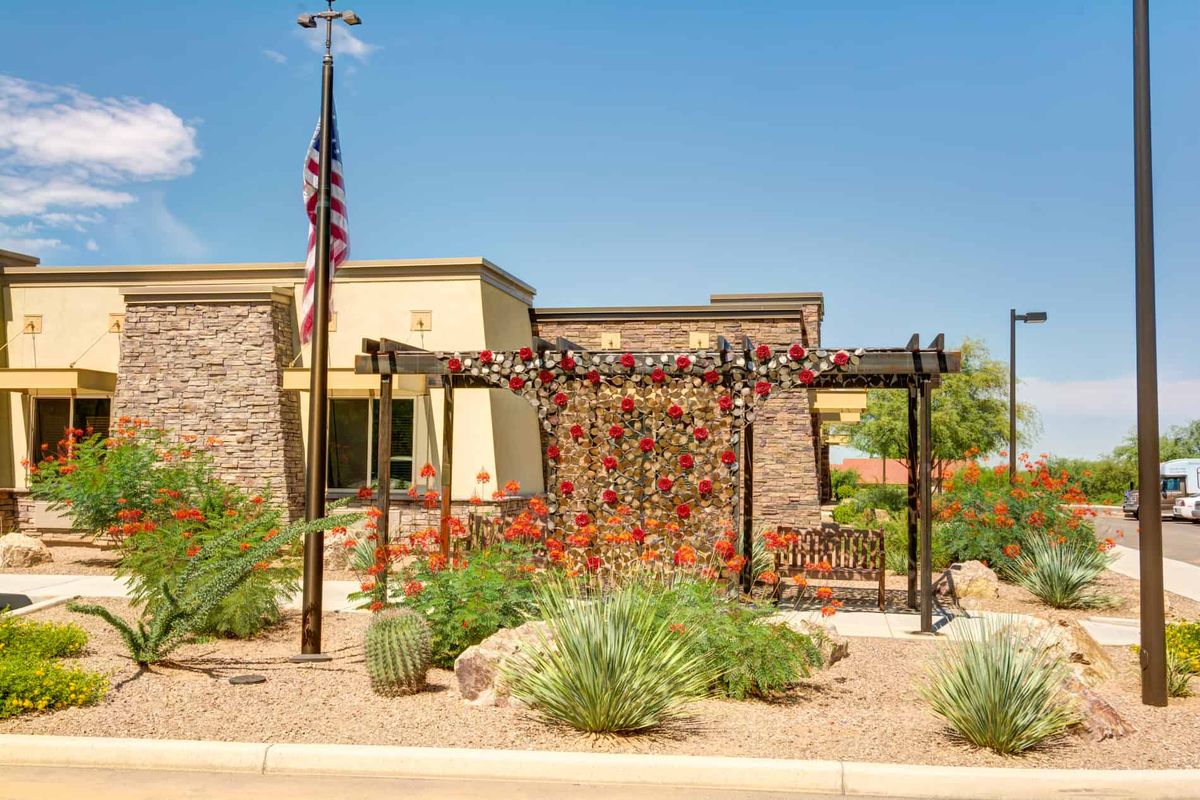 A building with a pergola and American flag in a landscaped area featuring desert plants on a sunny day.