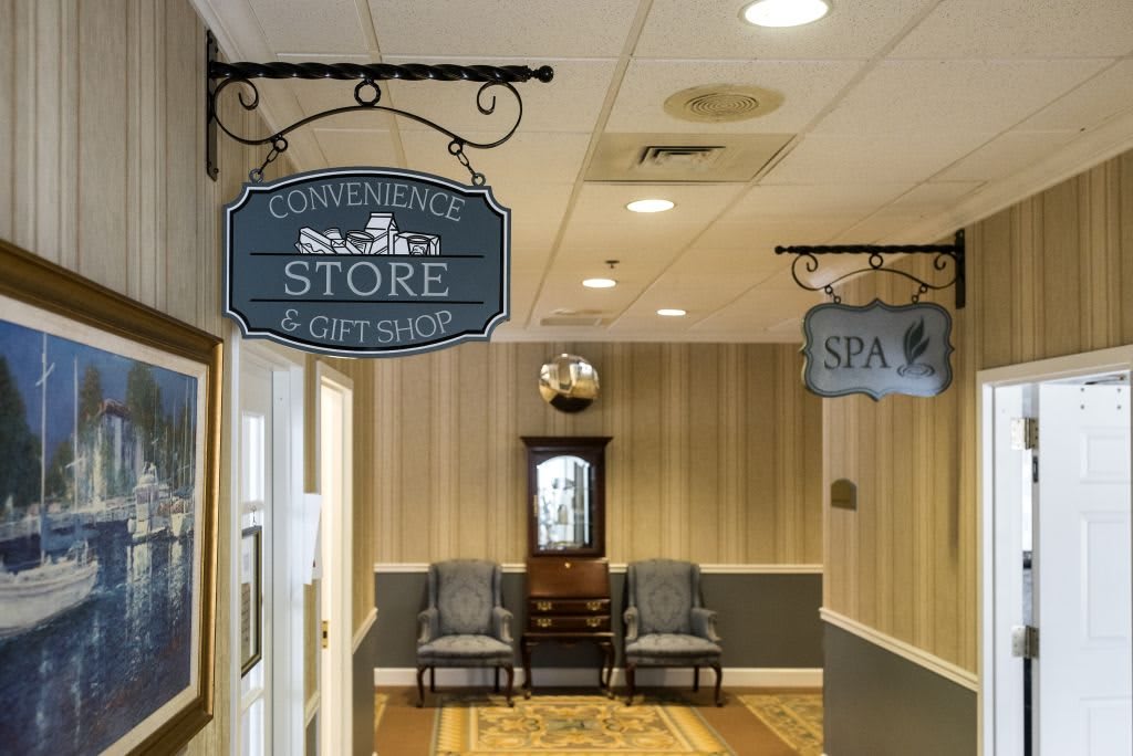 A hallway with signs pointing to a convenience store and spa, featuring a seating area with chairs and a decorative clock.