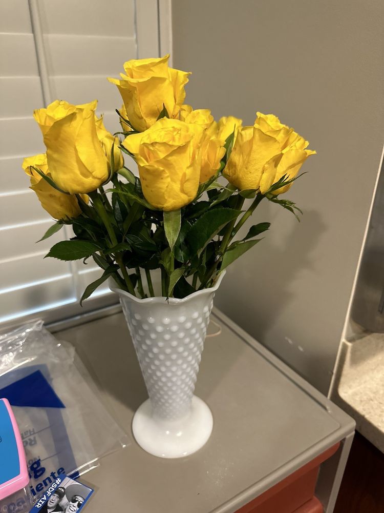 A bouquet of vibrant yellow roses in a white vase, elegantly placed on a table.