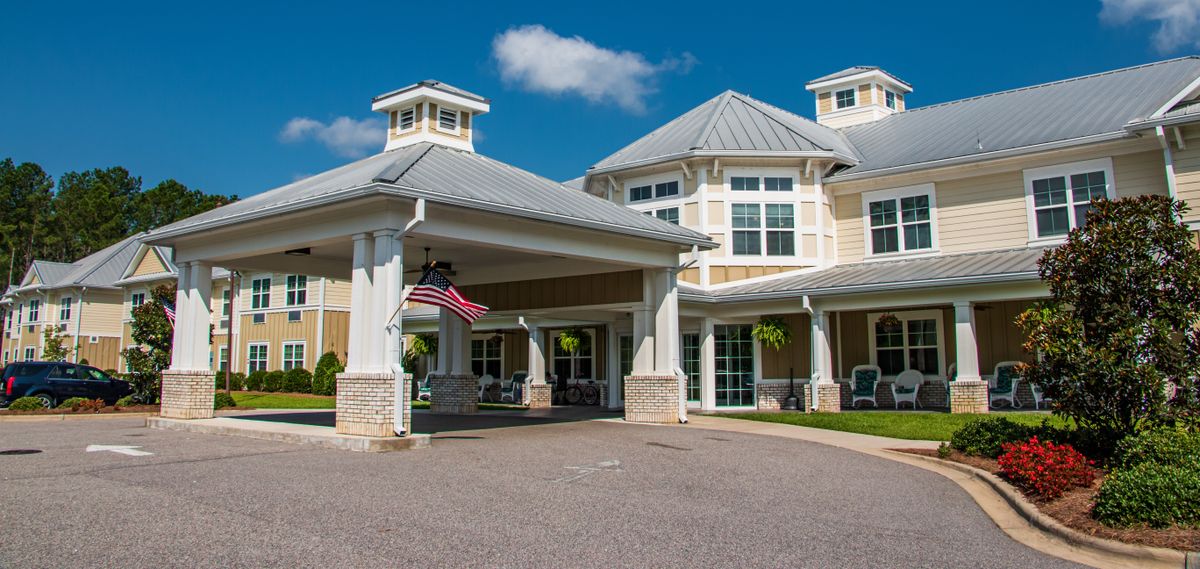 A large residential building with a covered entrance and an American flag, set against a clear blue sky.