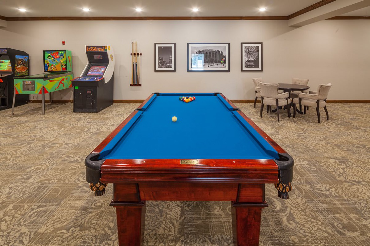 A game room featuring a blue-felt pool table and an arcade machine in the background.