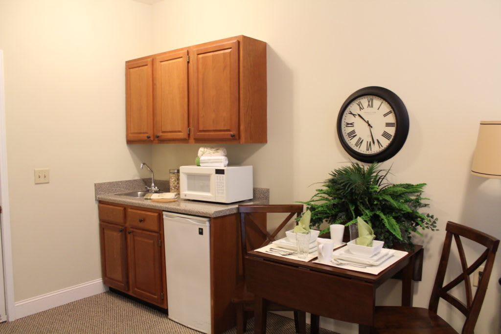 A kitchenette featuring wooden cabinets, a microwave, a sink, and a decorative clock on the wall.
