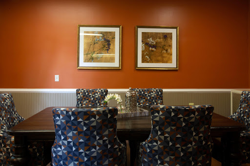 A cozy dining area featuring patterned chairs and framed artwork against an orange wall.