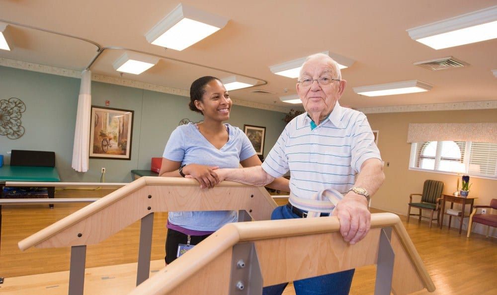 An elderly man receives assistance from a healthcare professional during physical therapy.