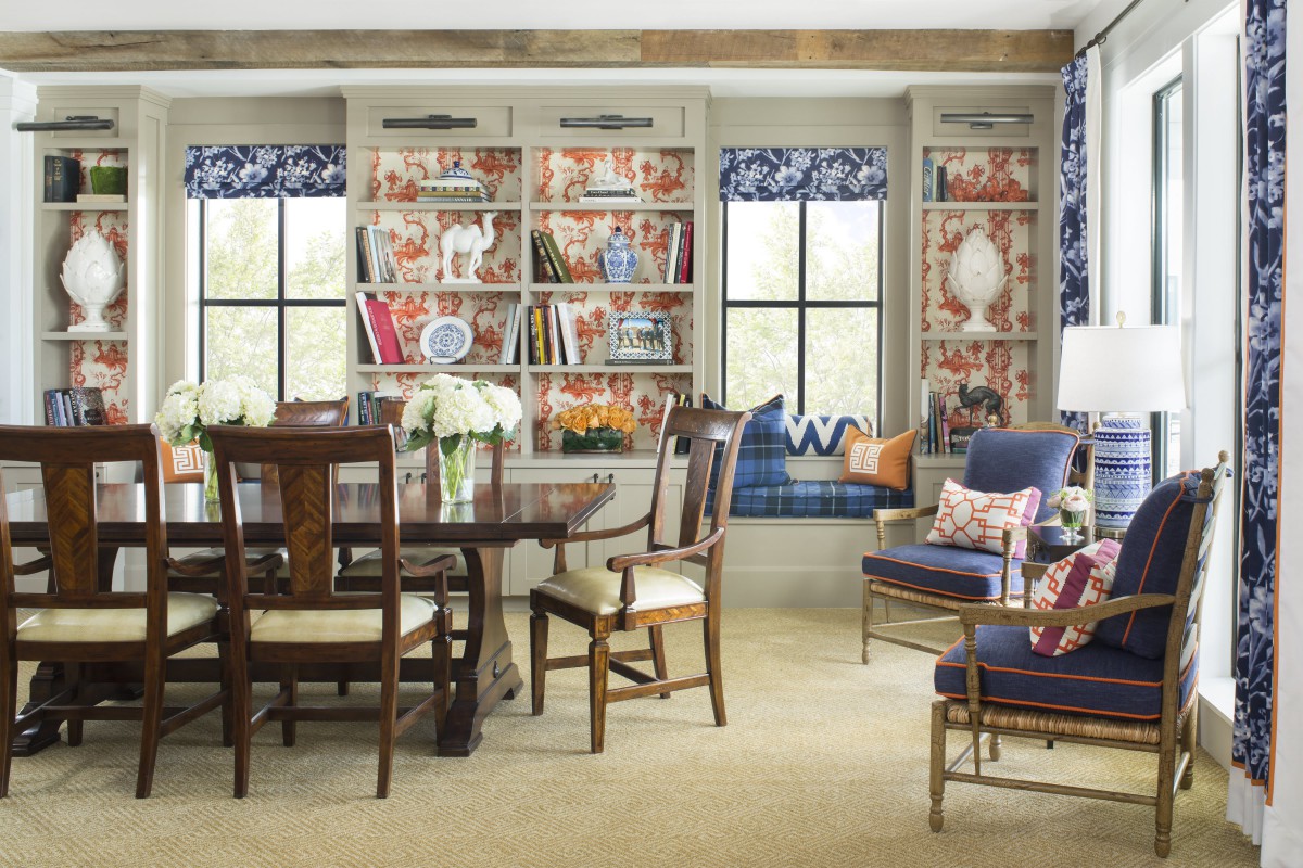 A cozy living room with a dining area, featuring bookshelves, a window seat, and colorful decor.