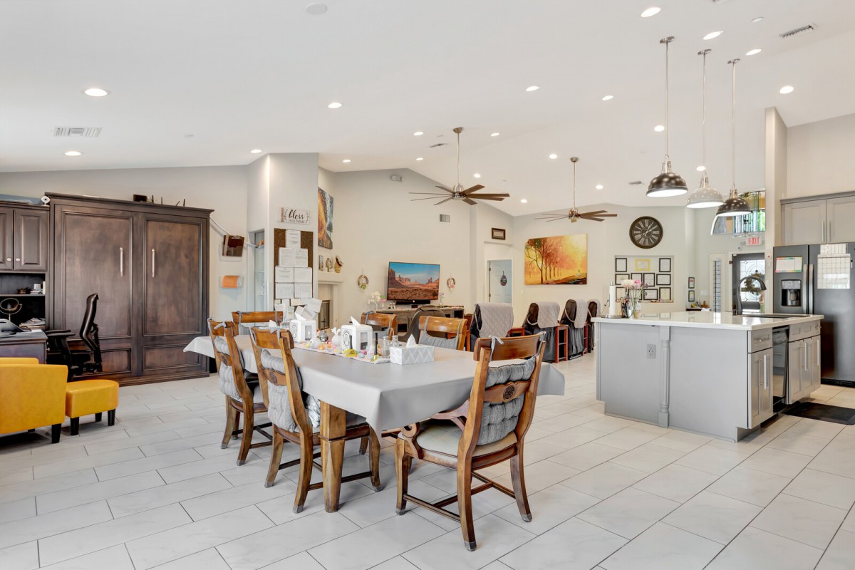 A modern and spacious open-concept dining area with a well-lit kitchen, featuring wooden chairs and artwork on the walls.