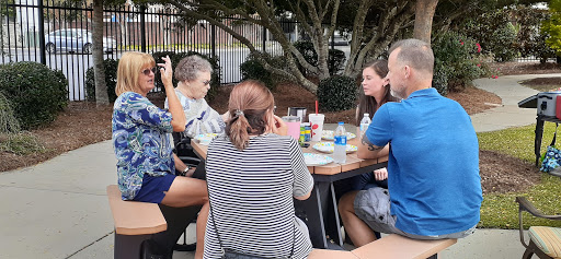 A group of friends enjoying a lively conversation over food and drinks at an outdoor table.