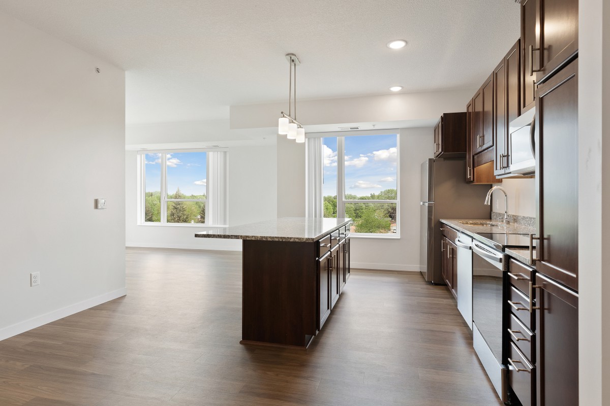 A modern kitchen featuring an island and large windows, with hardwood flooring and ample natural light.