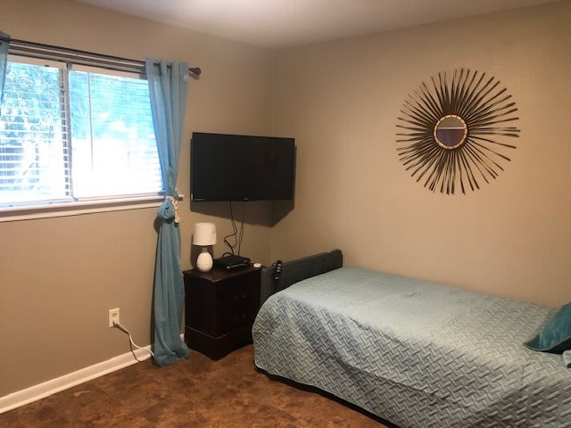 A cozy bedroom featuring a single bed, wall-mounted TV, and decorative wall art.
