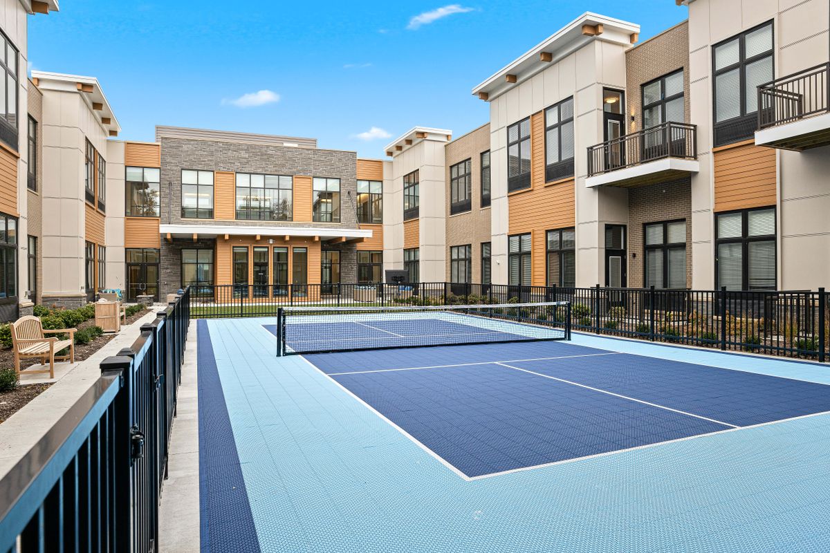 A modern residential complex featuring an outdoor tennis court under a clear blue sky.