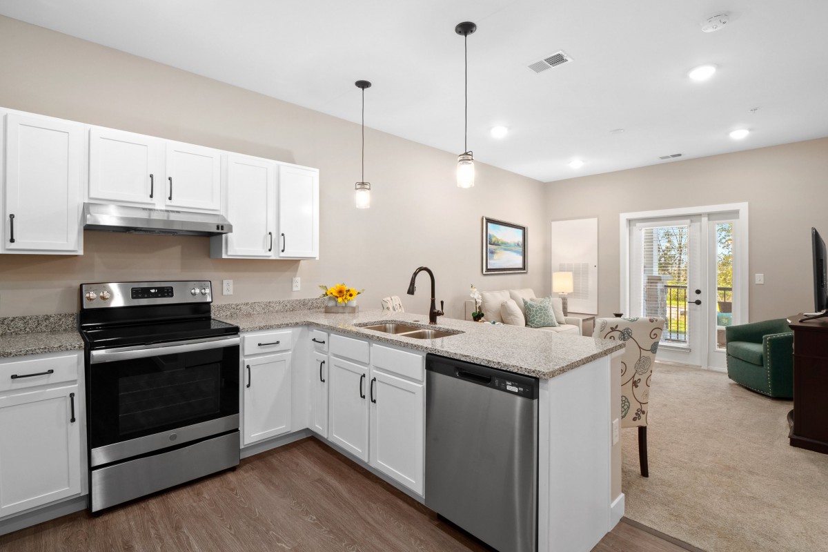 A modern kitchen with white cabinets and stainless steel appliances in an open-concept living space.