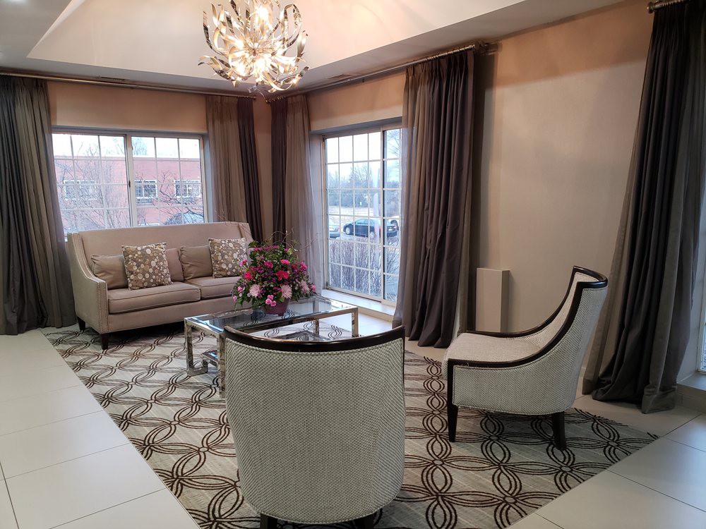 A stylish living room featuring a sofa, armchairs, and a modern chandelier, with large windows and elegant curtains.