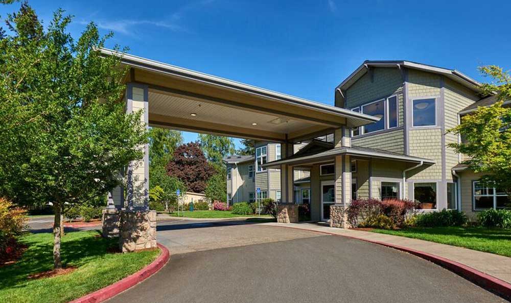 An inviting entrance with a covered driveway surrounded by lush landscaping and clear blue sky.