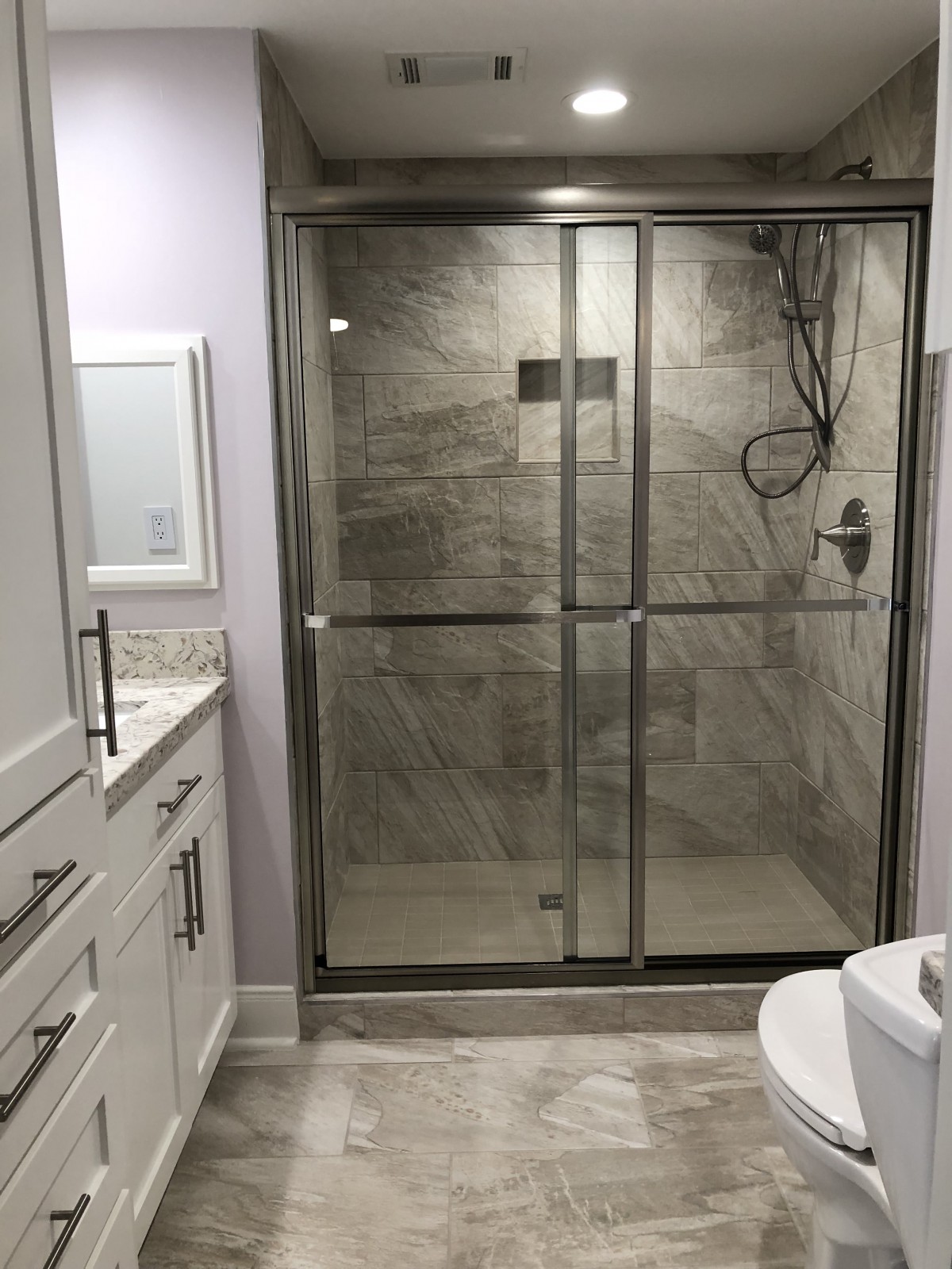 A modern bathroom with a tiled shower enclosed by glass doors and a vanity with drawers.