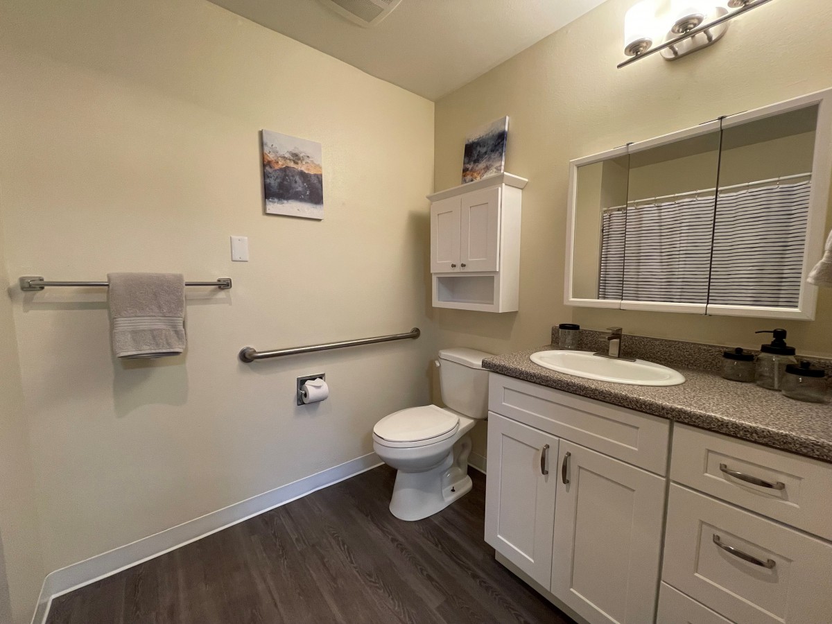 A clean and modern bathroom featuring a toilet, sink with cabinet, mirror, and towel rack.