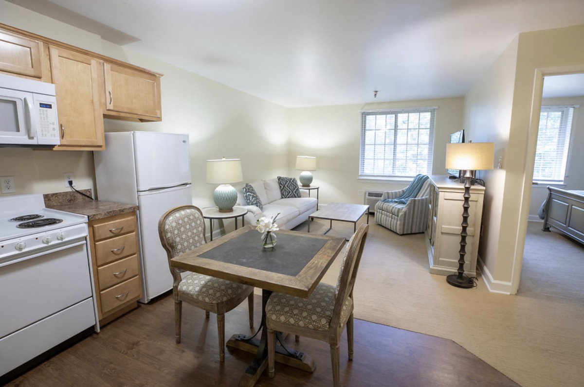 A cozy apartment with a dining area and living room featuring a table, chairs, sofa, and bright lighting.