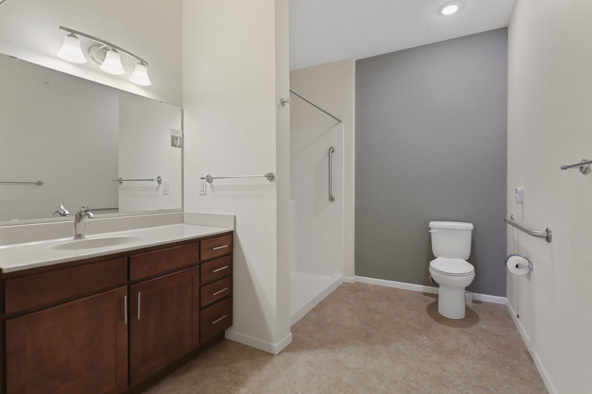 A modern bathroom featuring a toilet, vanity with a sink and mirror, and an enclosed shower area.