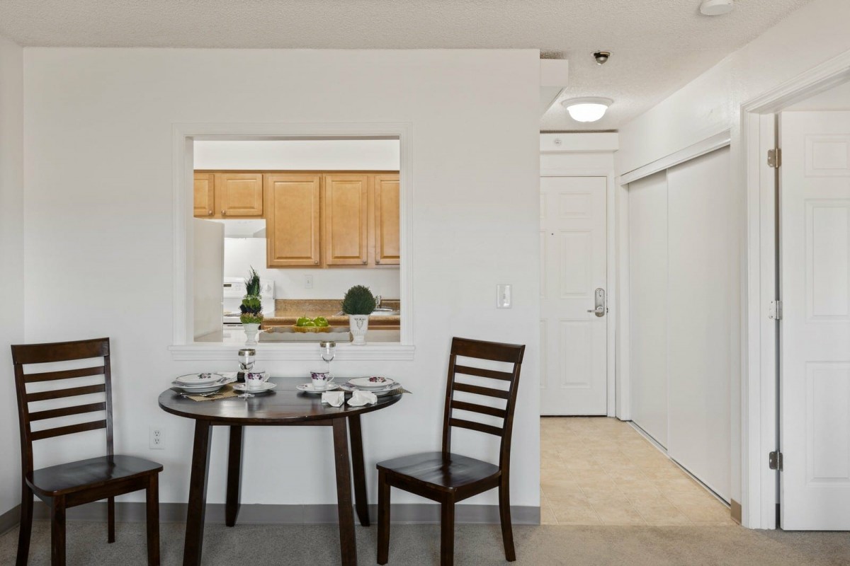 A minimalist dining area with a round table and two chairs, adjacent to a kitchen.