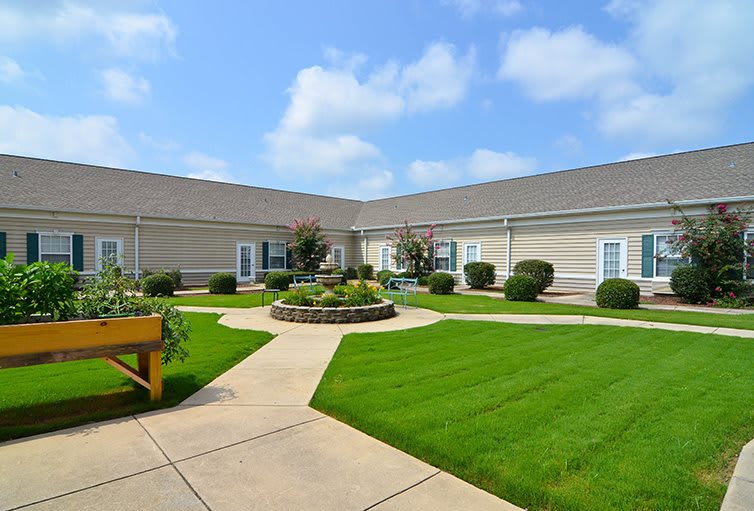 A well-maintained courtyard with green grass and a central garden, surrounded by a building under a clear blue sky.