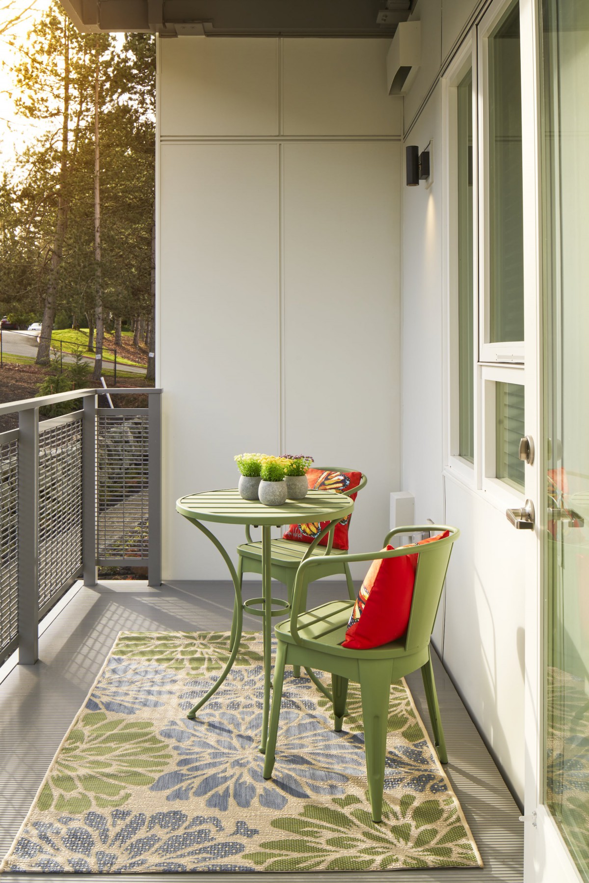 A cozy balcony with a small table and chairs, decorated with cushions and plants.