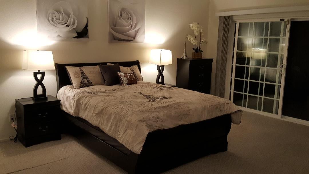 A cozy bedroom interior with a neatly made bed, soft lighting from a lamp, and decorative wall art.