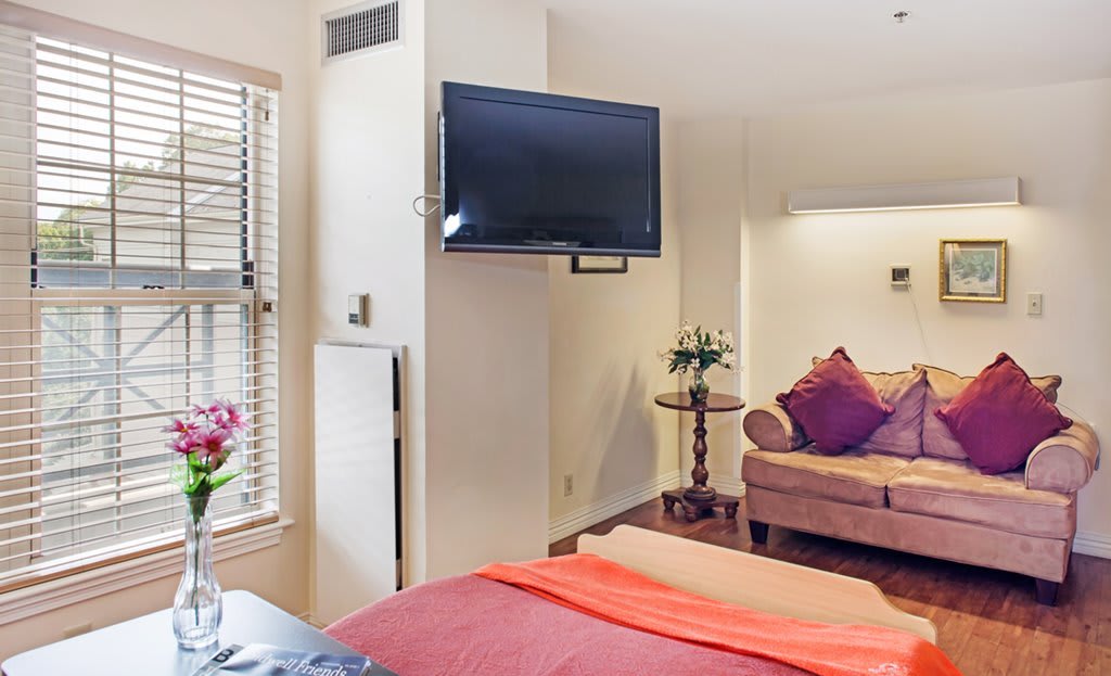 A cozy bedroom interior featuring a mounted television, comfortable sofa, and stylish decor.