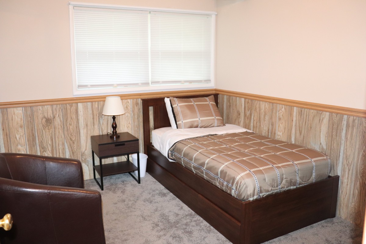 A cozy bedroom with a single bed, nightstand, and a chair.