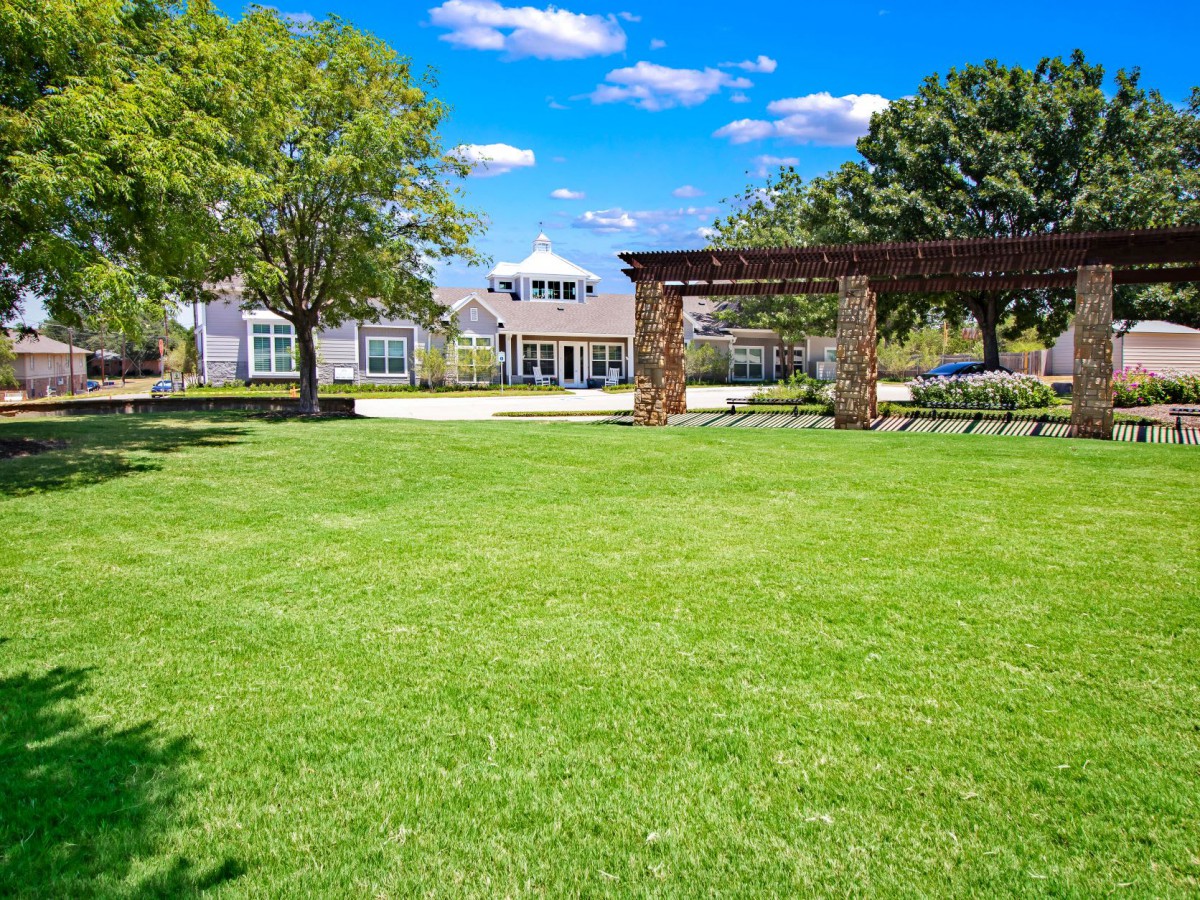 A beautiful garden with a lush green lawn and a house in the background under a clear blue sky.